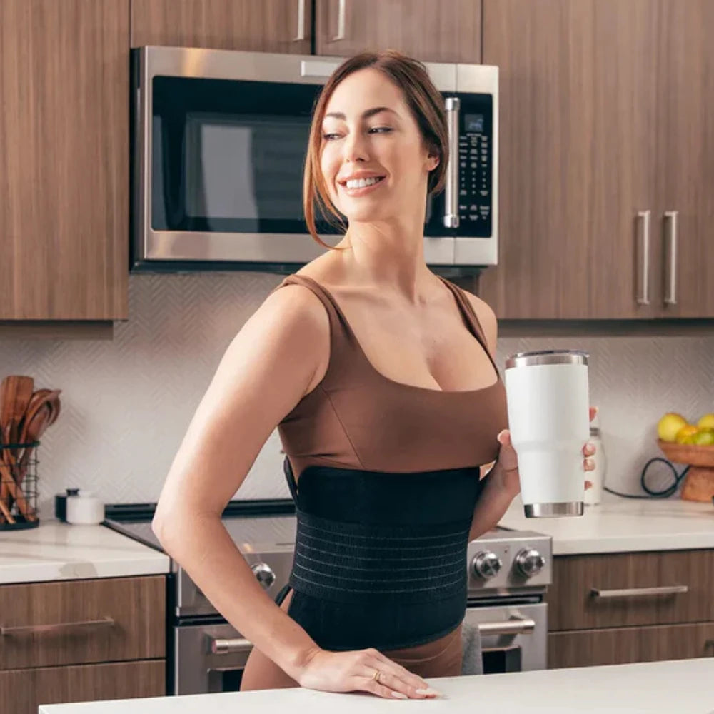 Smiling woman standing in a modern kitchen wearing the 360 LED Red Light Therapy Belt around her waist, appearing relaxed and comfortable while going about her daily routine.