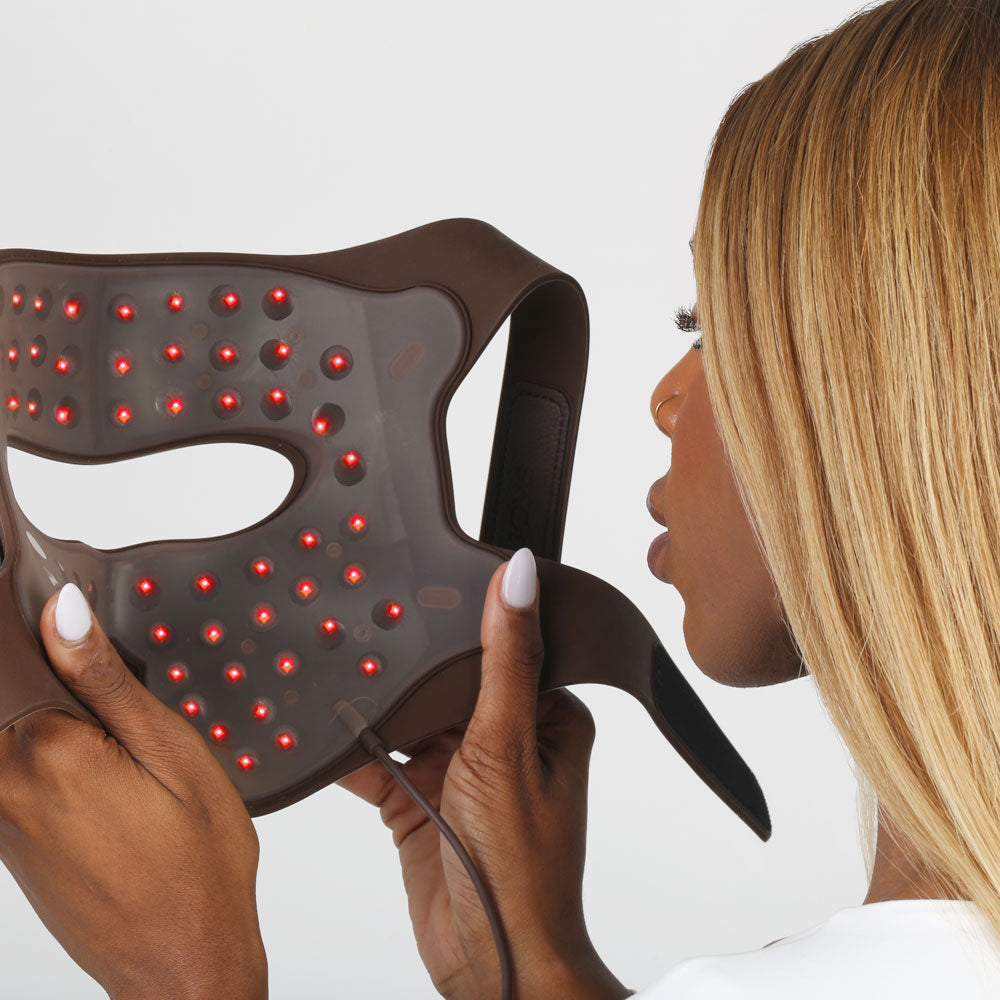 Woman holding the world's first re-nū 4D Laser Light Therapy Mask with red laser array, ready to revitalize her skin at-home.