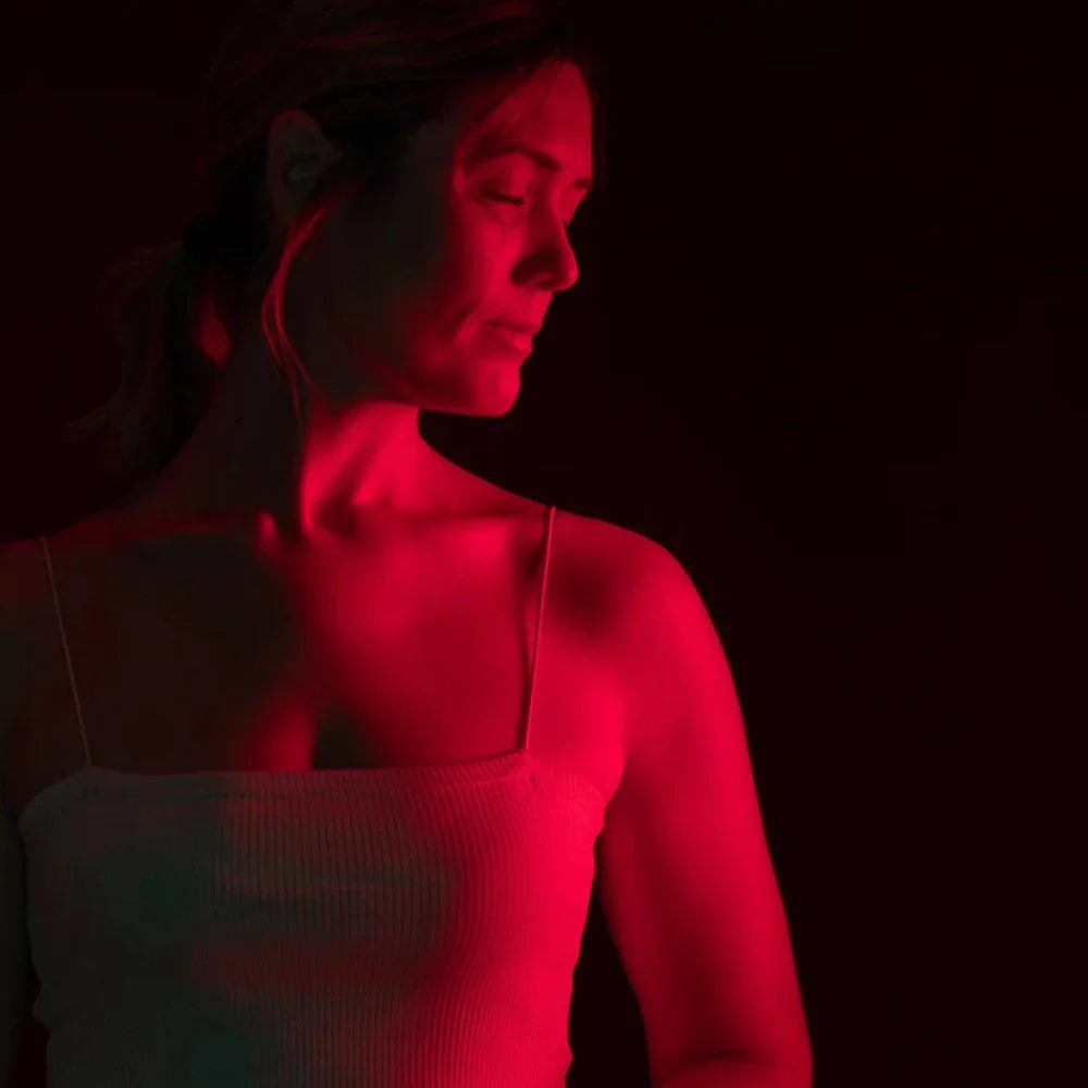 Woman using LED Red Light Therapy Panel with red light illuminating her face and neck during anti-aging treatment at home