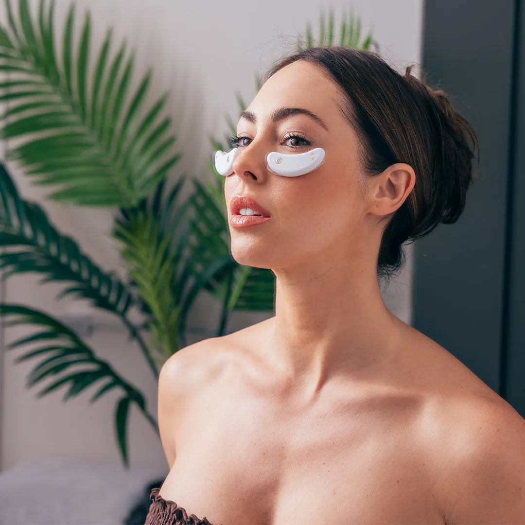 Woman wearing the GlowUp LED/EMS Under Eye Pads beneath her eyes, relaxing while the red light therapy activates for a targeted anti-aging treatment