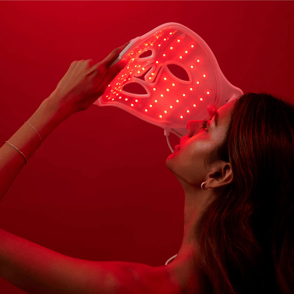 Woman gazing into the glowing red lights of the LED Beauty Mask by re-nū Smart Beauty, preparing to wear it for her skincare session