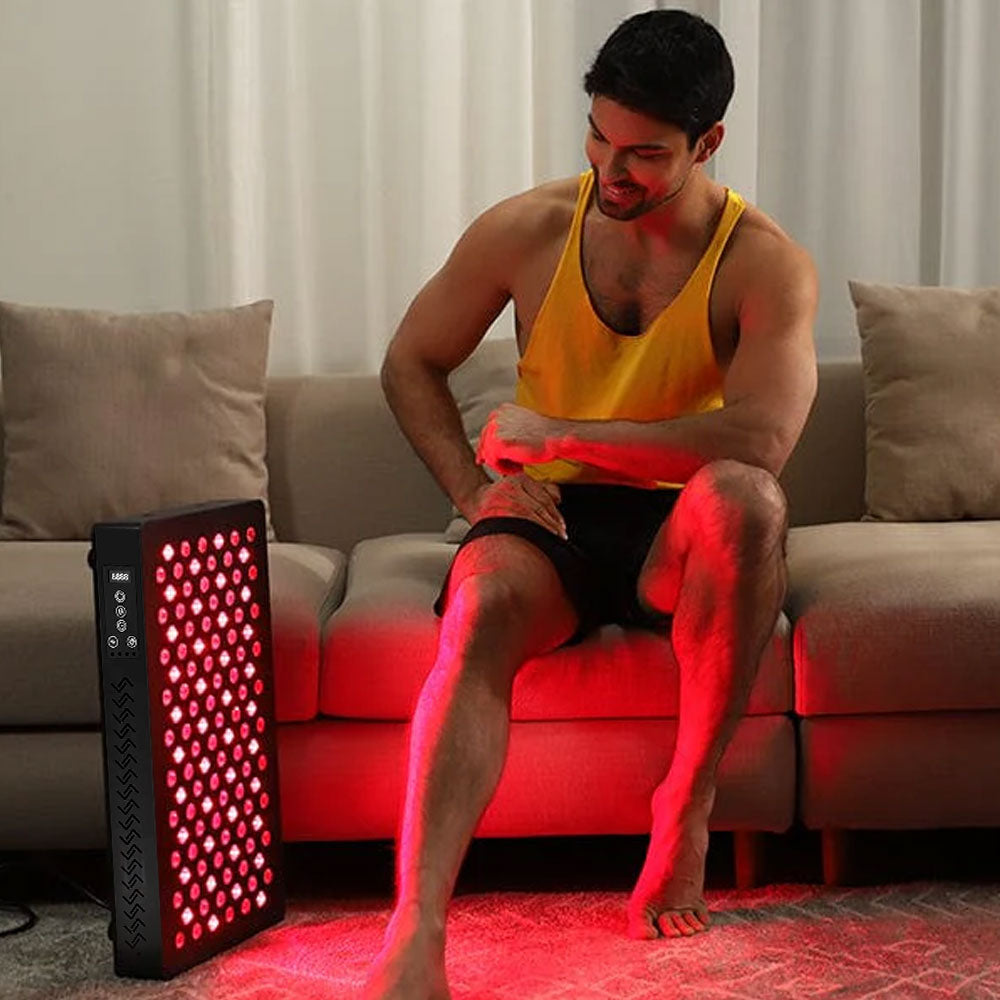 Man sitting on sofa using LED Red Light Therapy Panel Elite - Targeted Relief, looking relaxed and happy during light therapy session.
