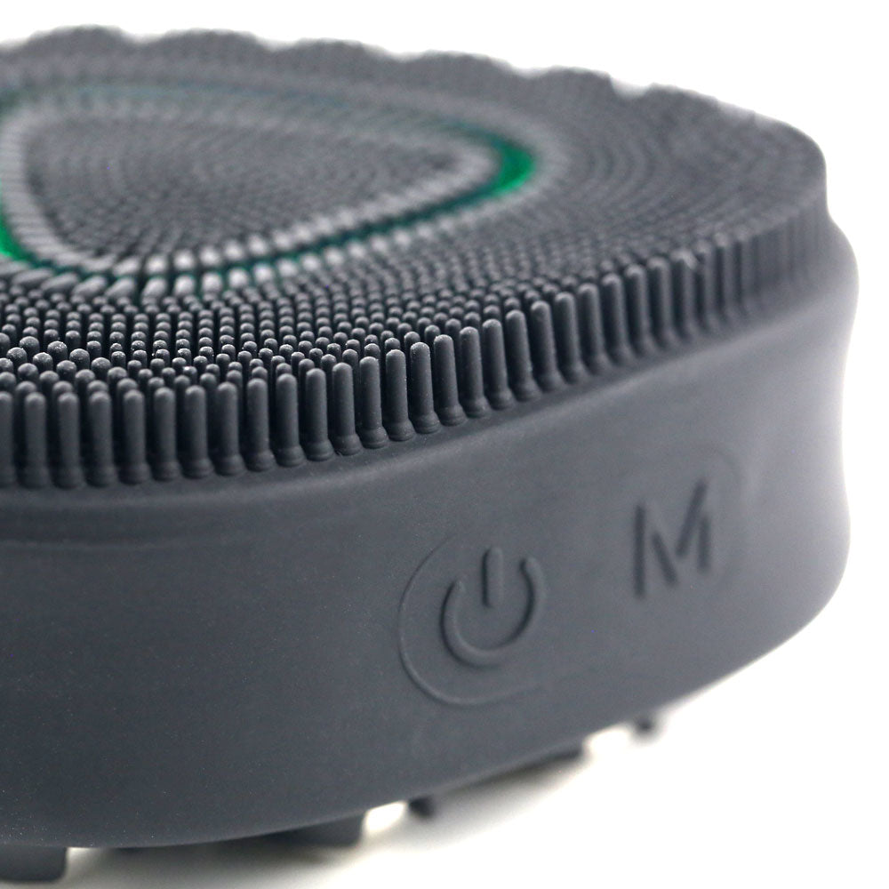 Close-up of the black PurePulse Pro Sonic Cleansing Brush with illuminated green LED light, showing textured silicone bristles and clearly visible power button for easy operation.