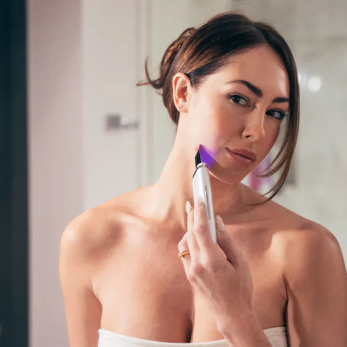 Woman using Ultrasonic Facial Scrubber along jawline with blue LED light for exfoliation and skin firming