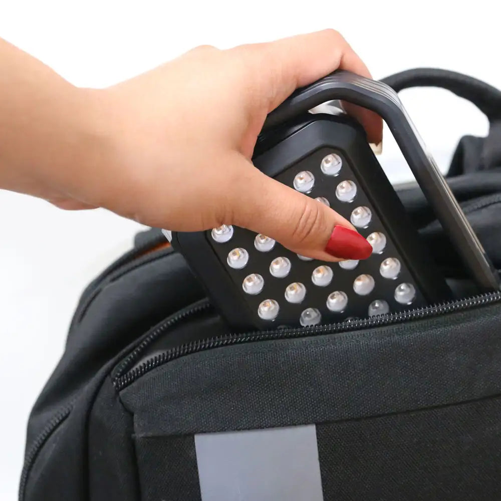 Woman’s hand sliding the UltraCompact LED Red Light Therapy Panel into a backpack pocket, demonstrating its lightweight, portable design.