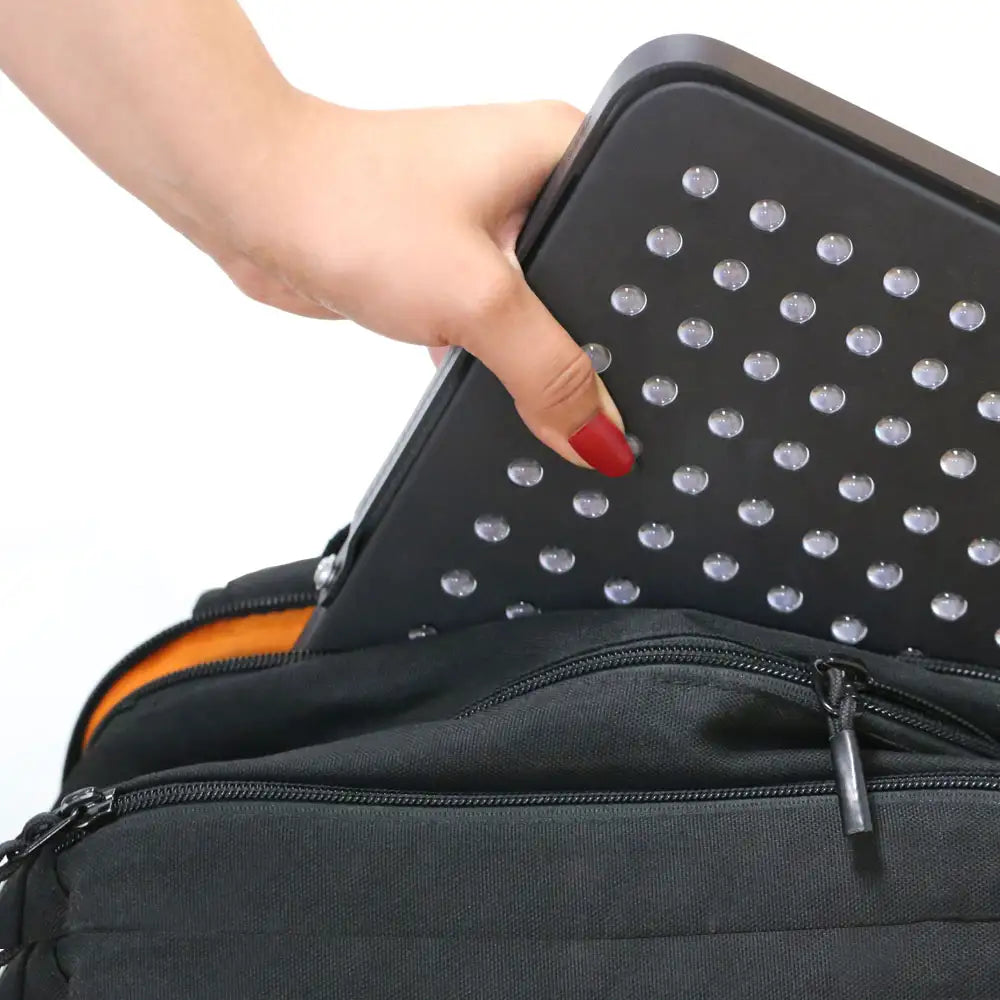 Woman’s hand sliding the UltraThin LED Red Light Therapy Panel into a backpack pocket, demonstrating its lightweight, portable design.