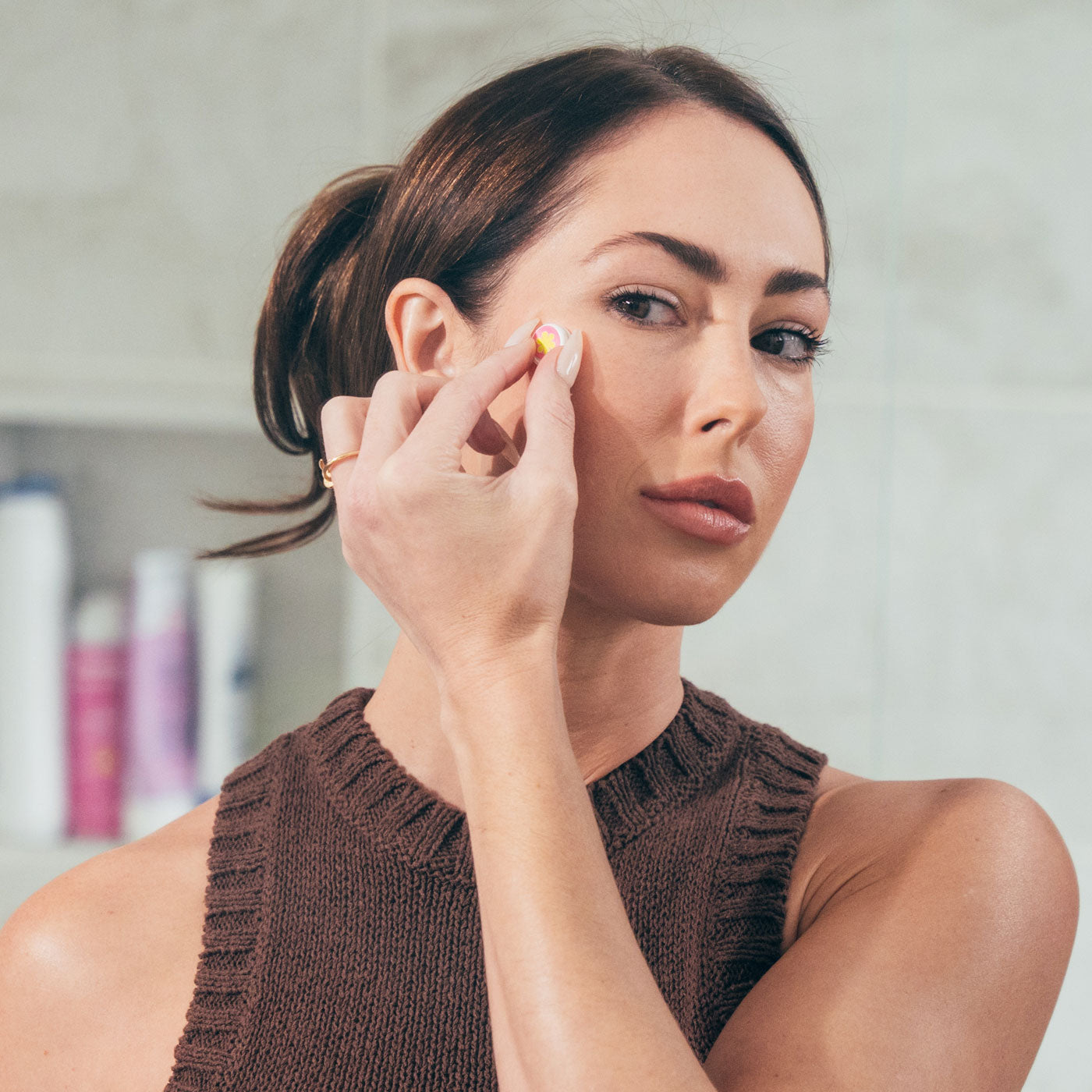 Woman with beautiful skin in front of a mirror while wearing the GlowUp Acne LED Patch on her right cheek for acne treatment.