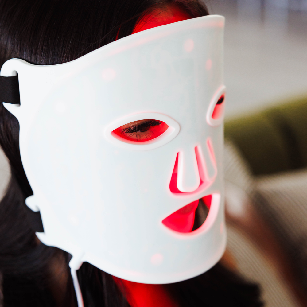 LED Beauty Mask worn by a woman at home, with red LED lights glowing, demonstrating its skin therapy effect.