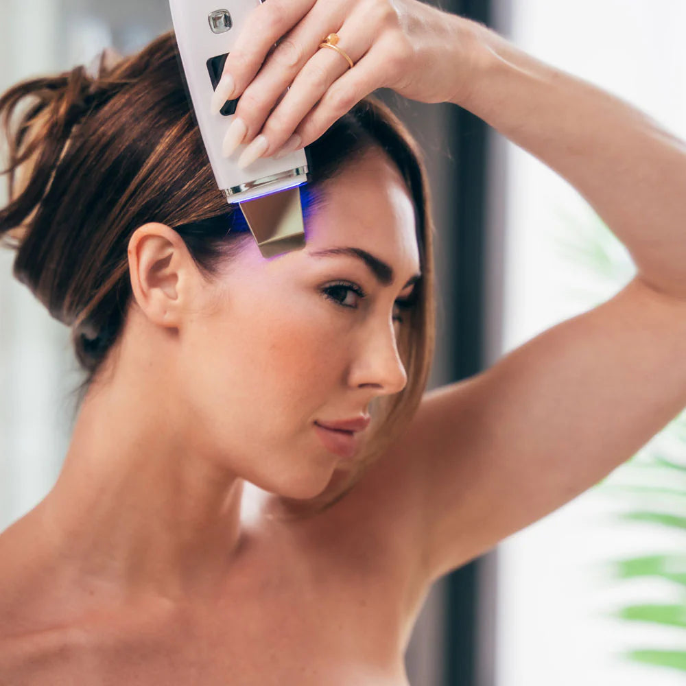 Woman exfoliating forehead with Ultrasonic Facial Scrubber using blue LED light for clearer skin and improved texture