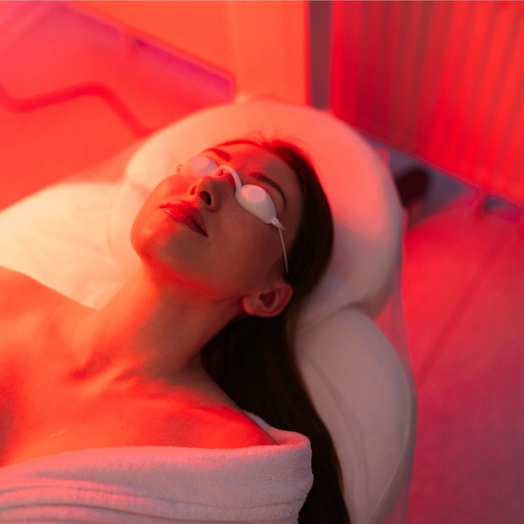 A woman receiving red light therapy in a serene spa room, focusing on skin care and relaxation.