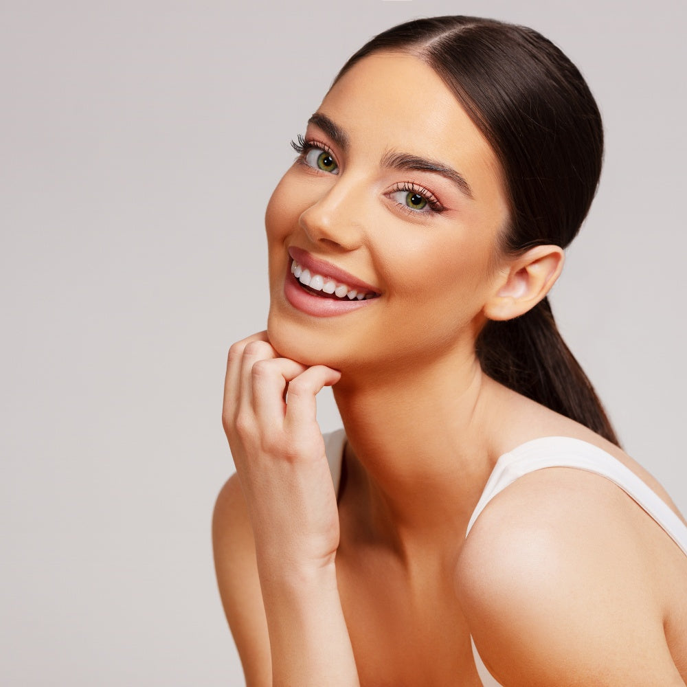 A beautiful woman smiles with her hands on her chin, showcasing the effects of Mask LED Light Therapy on her skin.