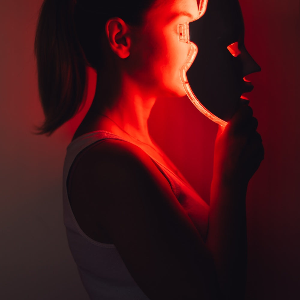 A woman holds a mask emitting red light, showcasing the benefits of LED light therapy for skin rejuvenation.