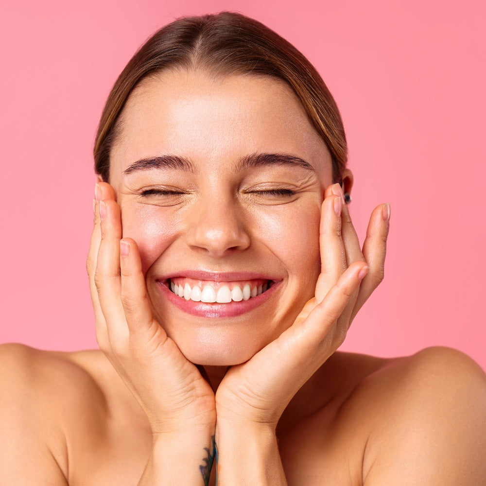 A woman smiling with her hands on her face, enjoying the benefits of LED light therapy for her skin.