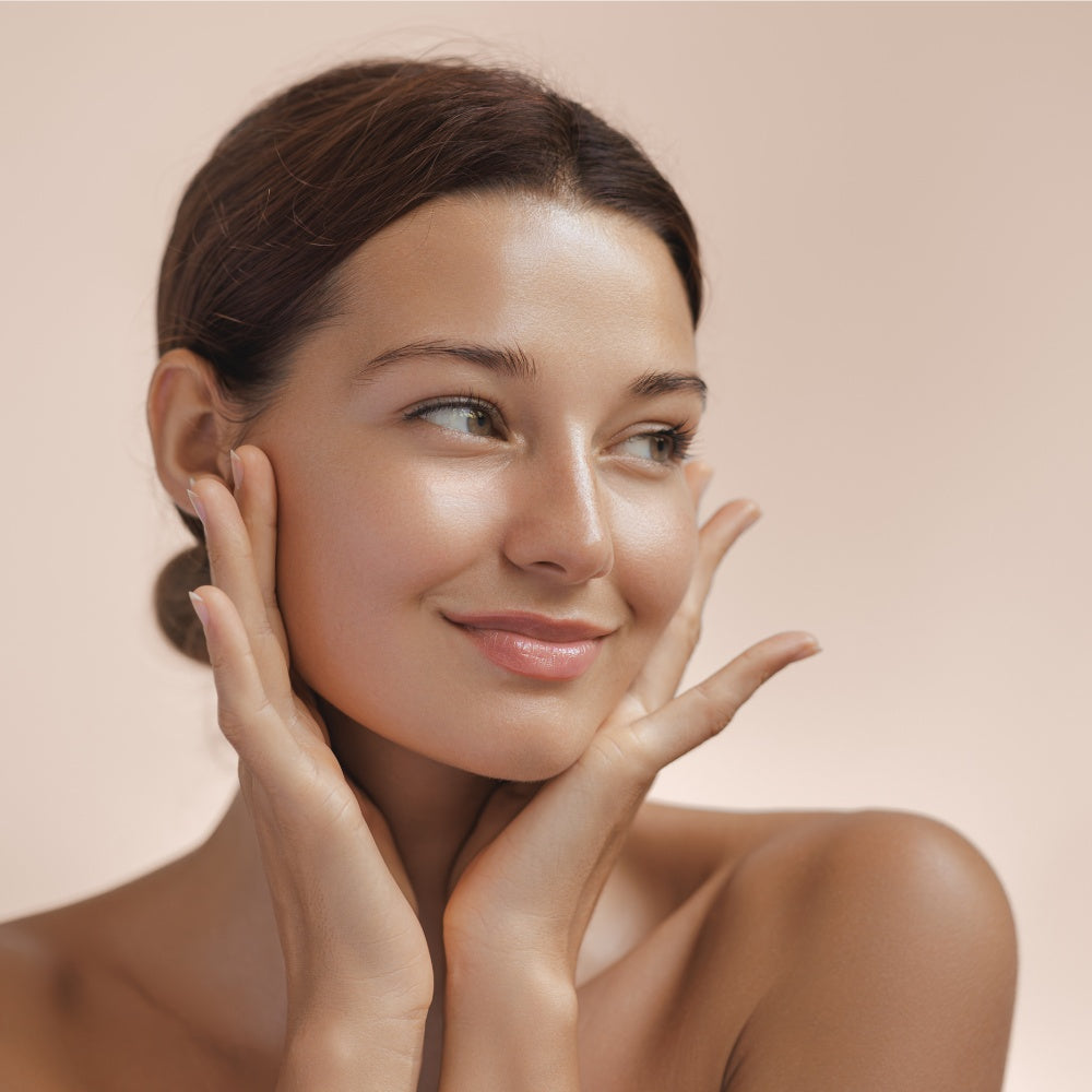 A woman with a clean face gently touching her cheeks, showcasing the benefits of LED light therapy for skin rejuvenation.