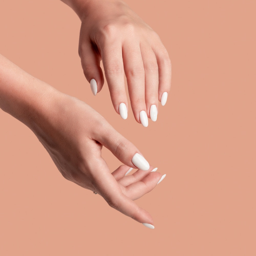 Hands with white manicured nails resting on a peach background, showcasing the soothing effects of Mask LED Light Therapy.