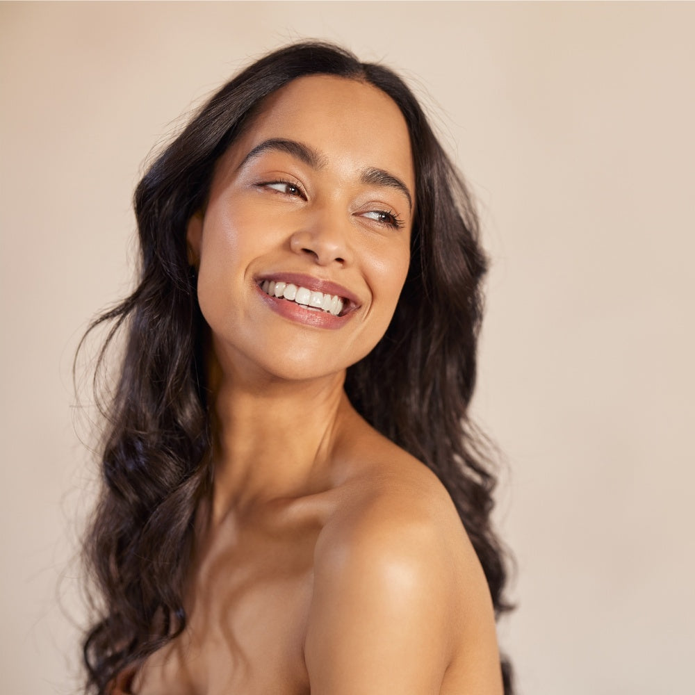 A woman with long hair smiles warmly, radiating joy and positivity in a bright setting.