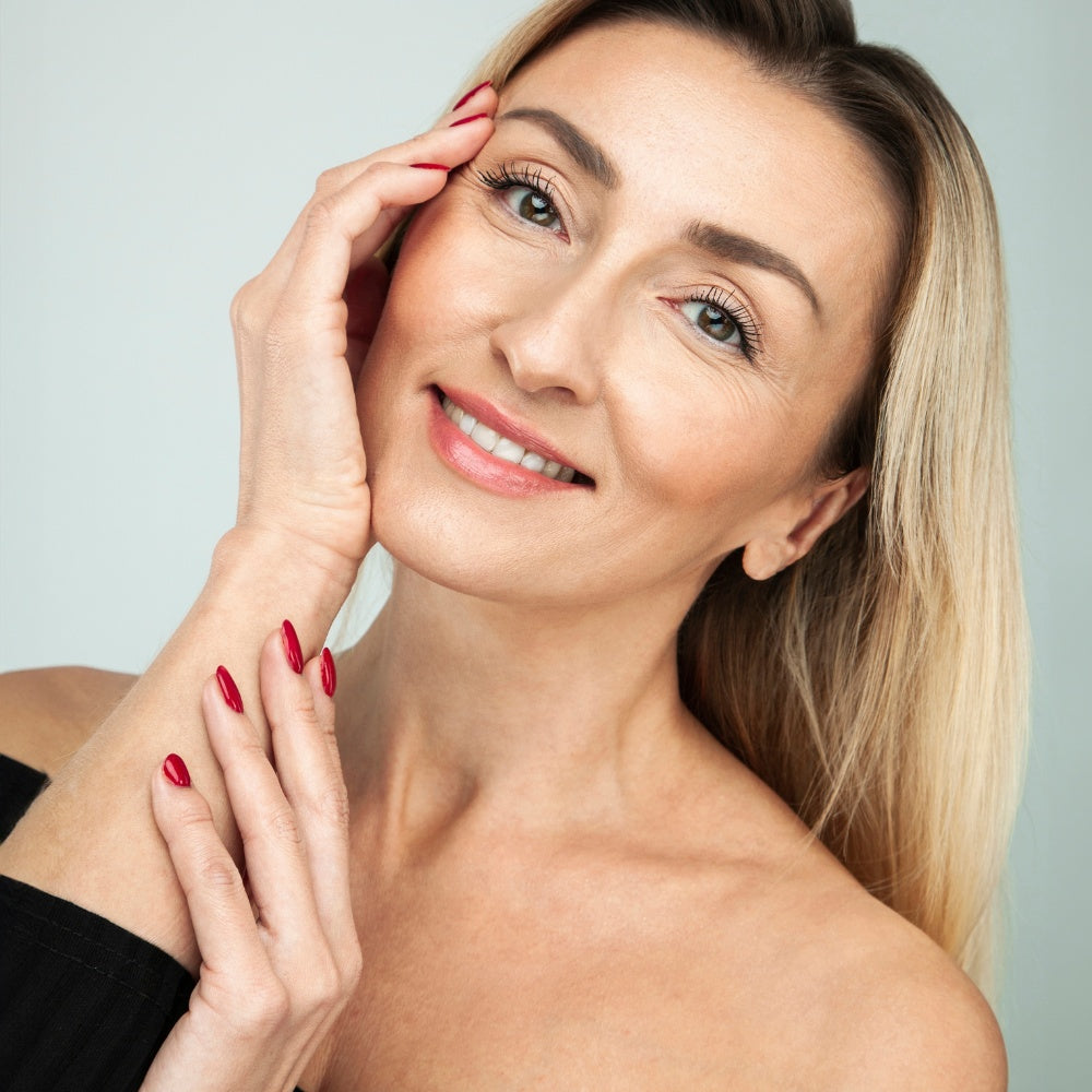 A woman with long blonde hair and red nails using a Mask LED Light Therapy device for skincare treatment.