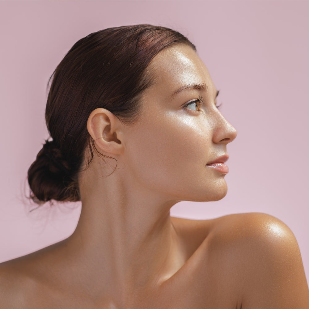 A woman with an exposed upper body gazes upward, enhanced by the glow of a Mask LED Light Therapy treatment.