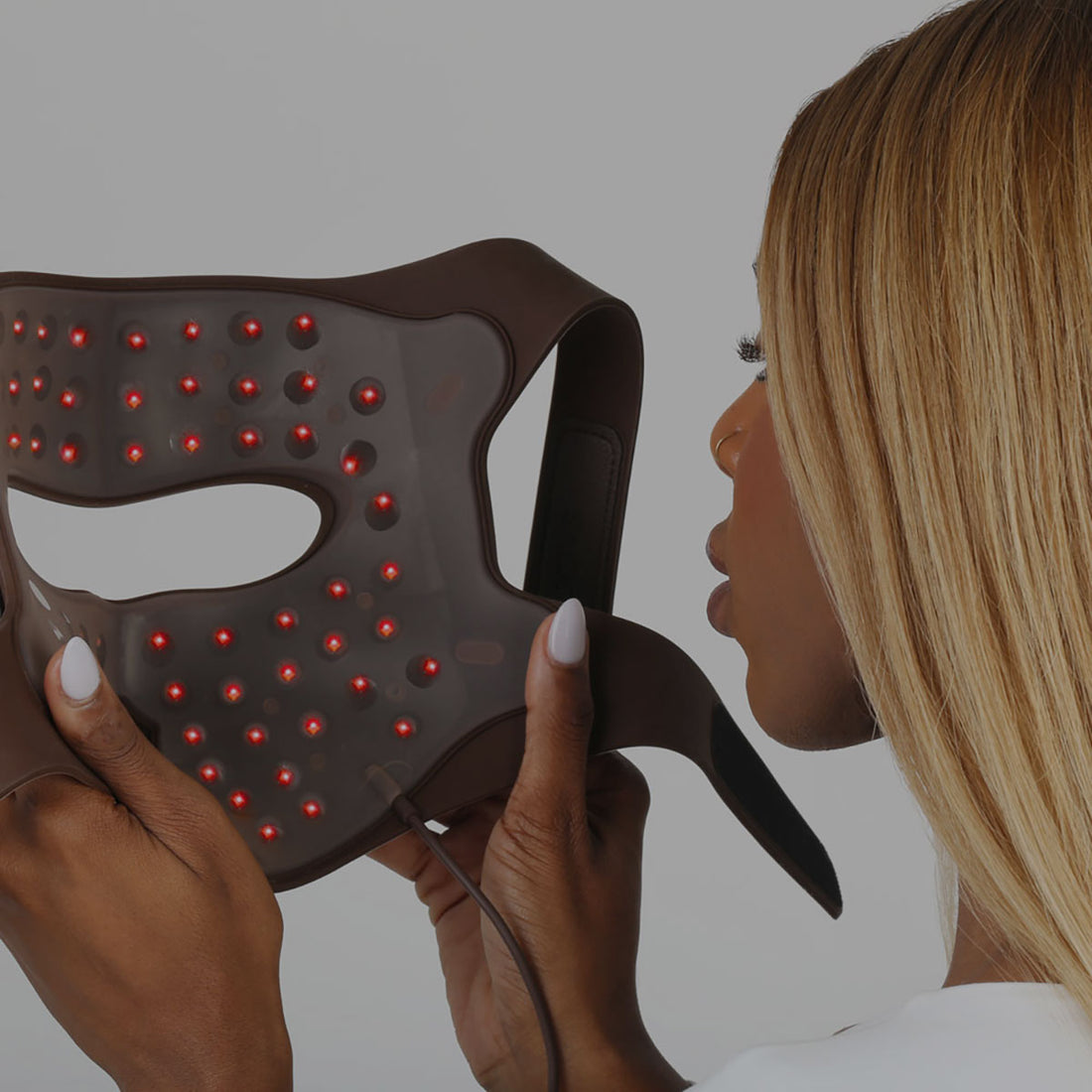 Woman holding the world's first FDA-cleared 4D Laser Light Therapy Mask with red lights against a gray background.
