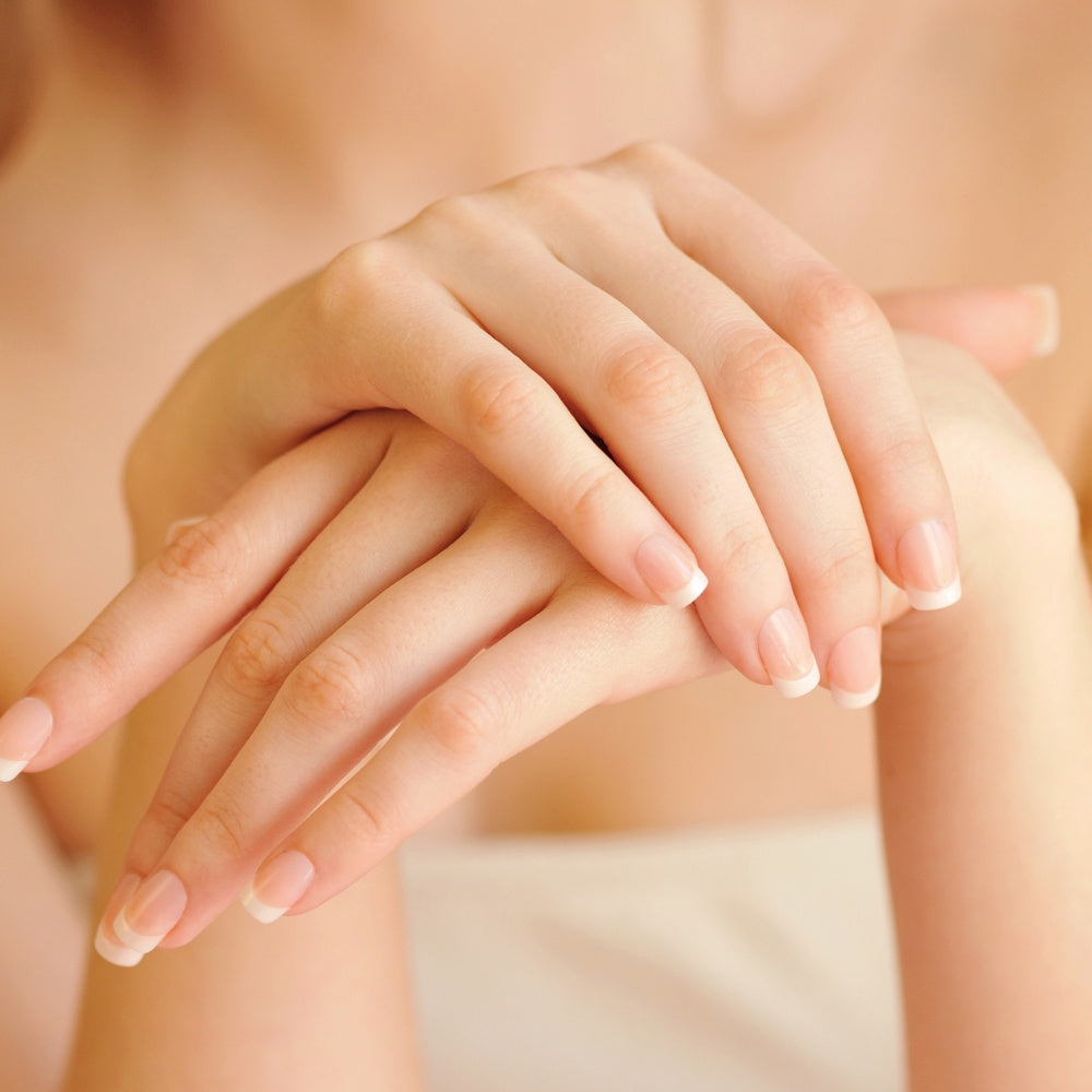 A woman with long nails and fair skin undergoing LED light therapy treatment with a mask on her face.