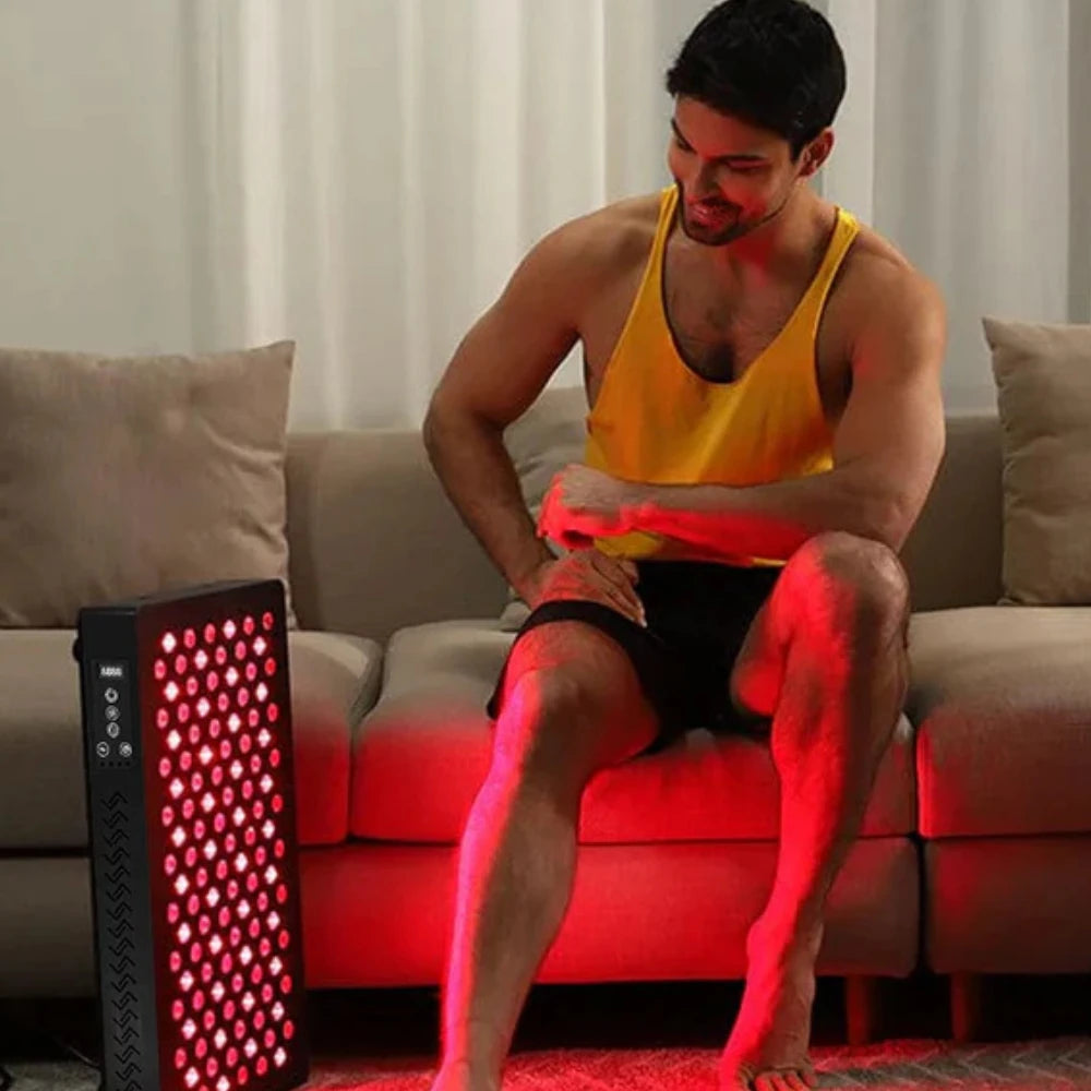 Man sitting on sofa using LED Red Light Therapy Panel Elite - Targeted Relief, looking relaxed and happy during light therapy session