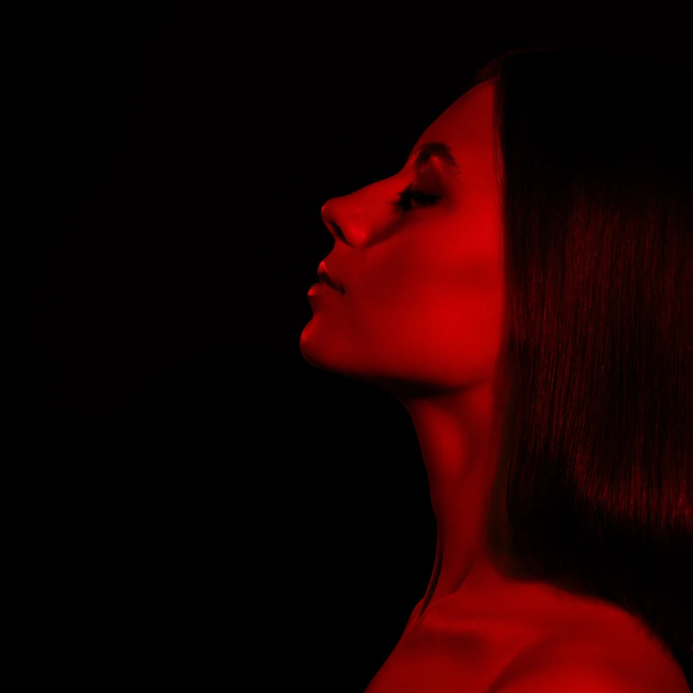 Girl using LED Red Light Therapy Panel Elite - Targeted Relief with eyes closed and red light illuminating her neck and face, showing calm and relaxed facial expression
