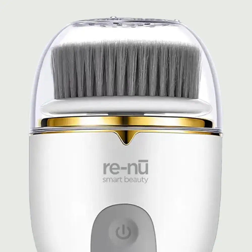 Close-up of re-nū Smart Beauty PureSpin Facial Cleansing Brush showing ultra-soft gray bristles, gold accent ring, and protective cap for hygienic storage
