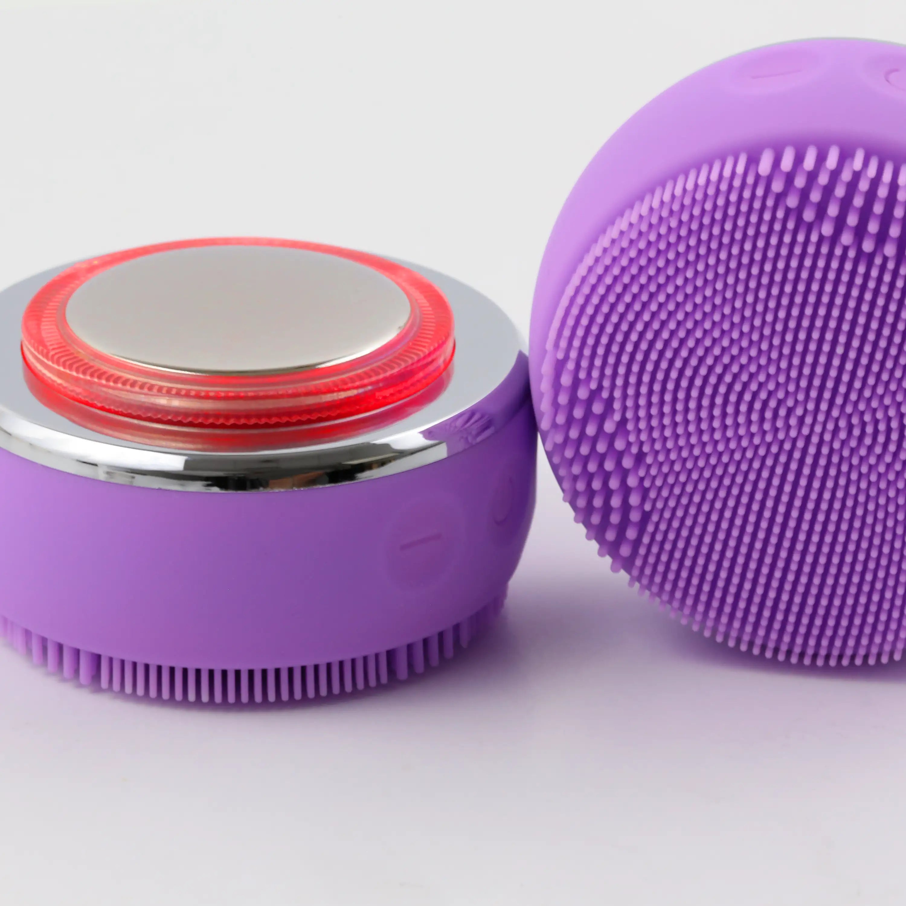 Close-up of the PurePulse Pro Plus chrome EMS head with red LED illumination beside a second brush resting on its side showcasing the soft silicone bristles