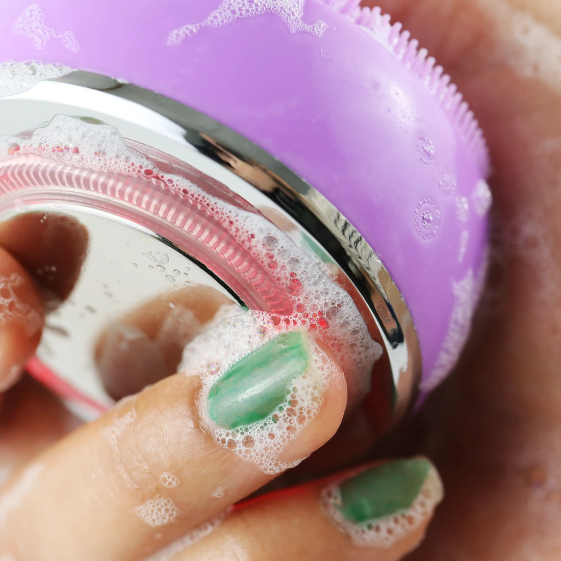 Hand holding the PurePulse Pro Plus Sonic Cleansing Brush covered in rich cleansing foam with silicone bristles visible and water-resistant design ready for use