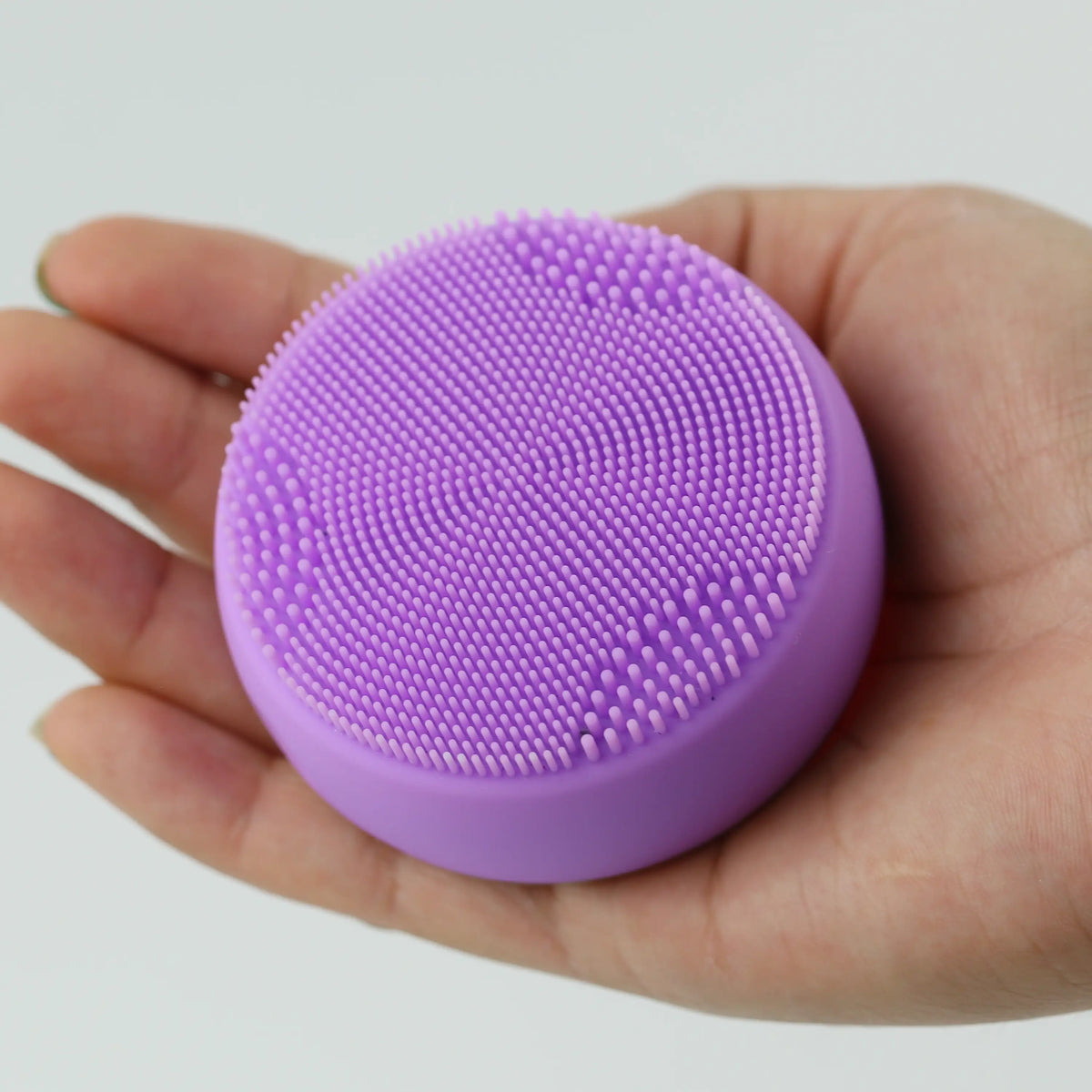 Hand holding the PurePulse Pro Plus Sonic Cleansing Brush in the palm with silicone bristles facing upward, highlighting compact size and ergonomic grip