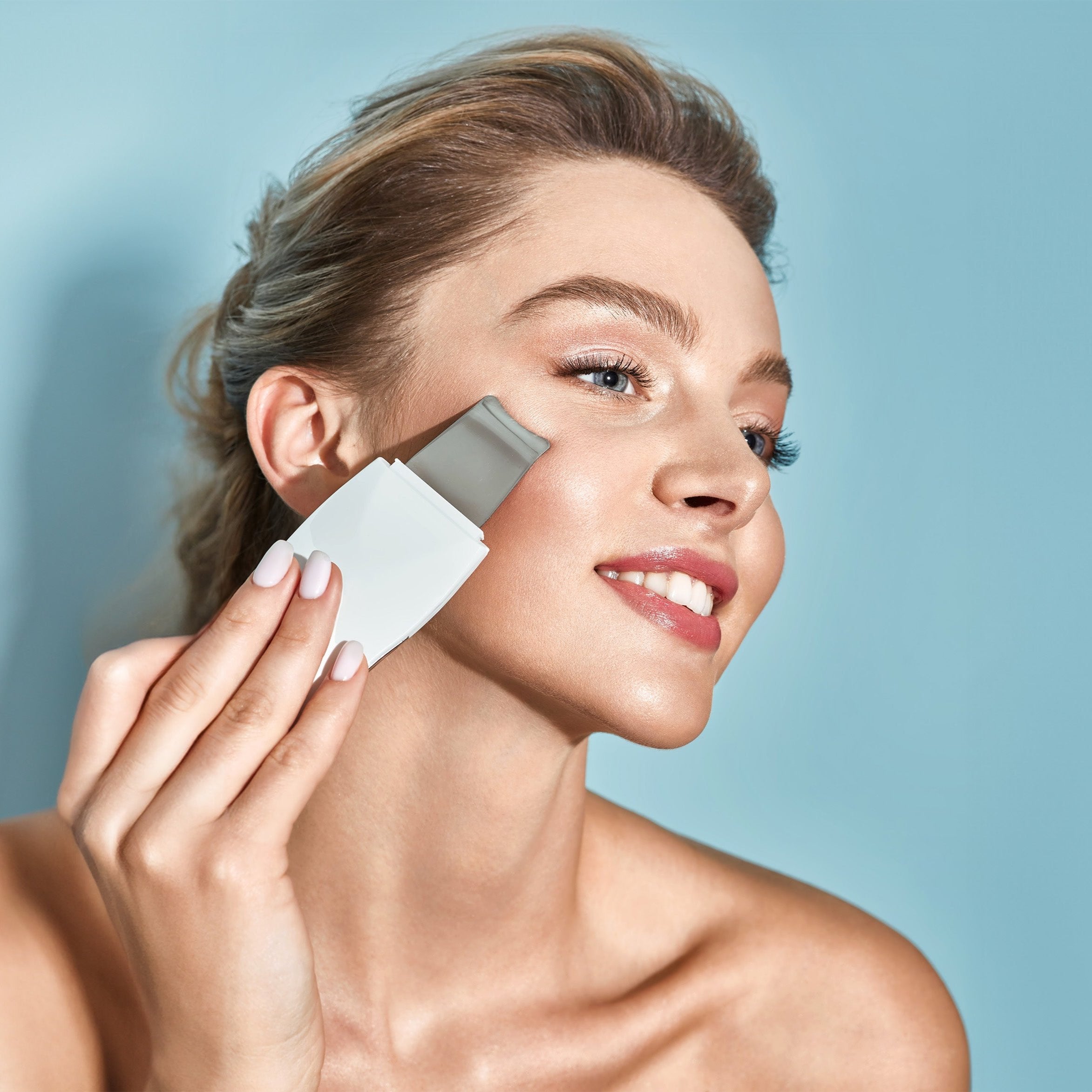 A woman cleans her face with a facial brush, utilizing an ultrasonic scrubber on a wireless charge base.