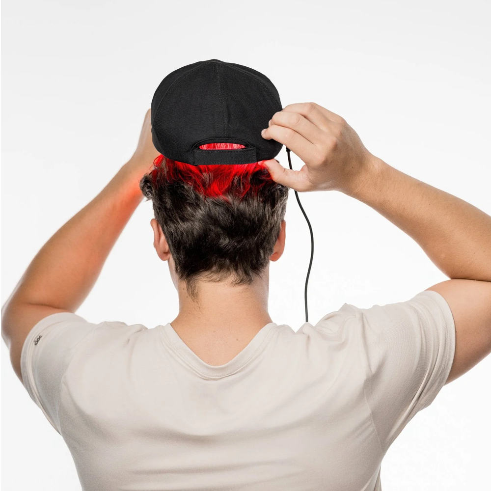 A man adjusts his hat while undergoing red light hair therapy, showcasing a modern approach to hair restoration.