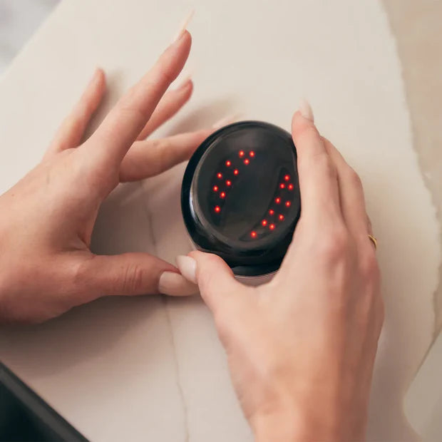 Close-up of a hand opening the GlowUp Under Eye Pads charging case, with red LED light visibly activated inside, indicating the pads are charging and ready for use.