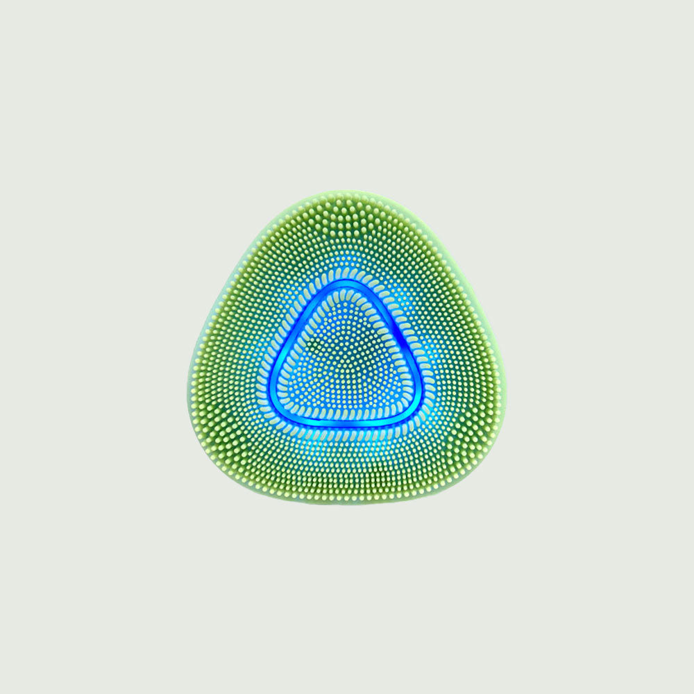 Close-up of a green triangular sonic cleansing brush featuring soft silicone bristles and a glowing blue LED light ring, designed for deep facial cleansing and exfoliation