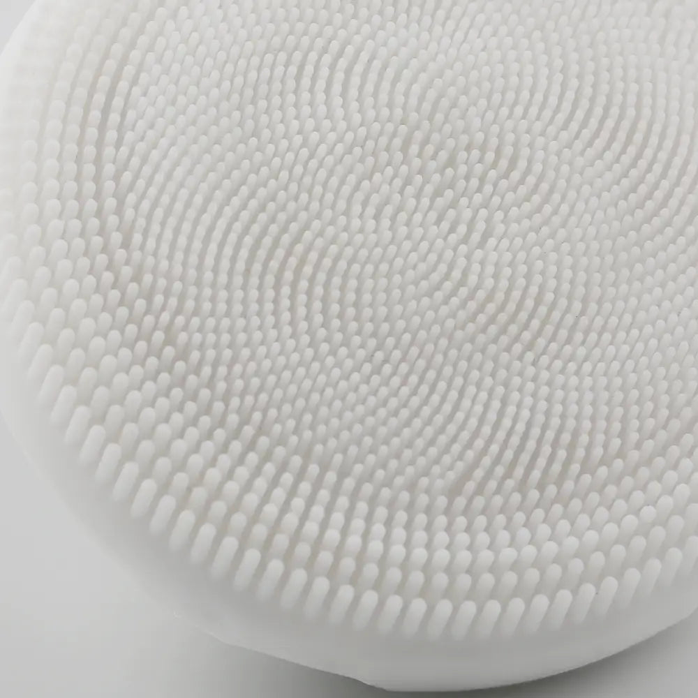A close-up view of the PurePulse Sonic Cleansing Brush showing it's textured bristles and a silver ring handle, for deep pore cleansing and gentle exfoliation.