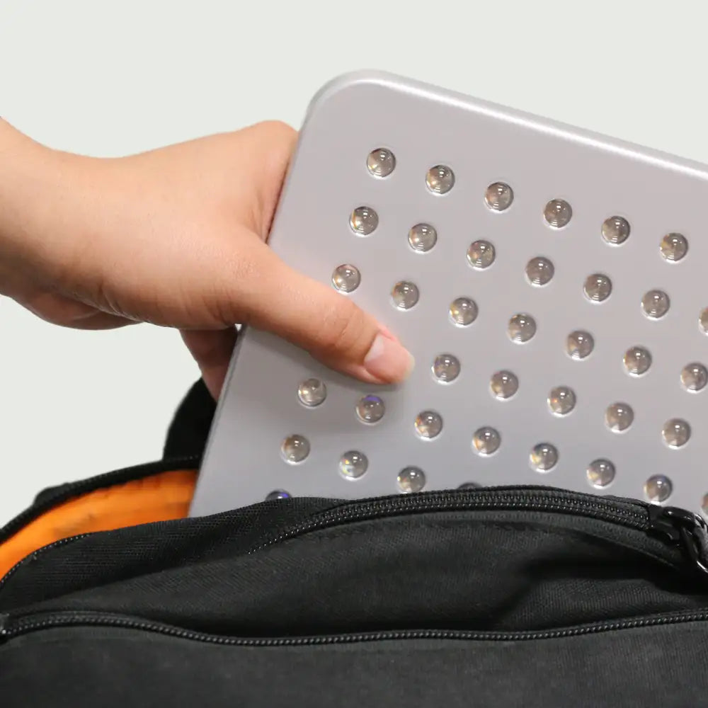 Woman’s hand sliding the UltraThin LED Red Light Therapy Panel into a backpack pocket, demonstrating its lightweight, portable design.