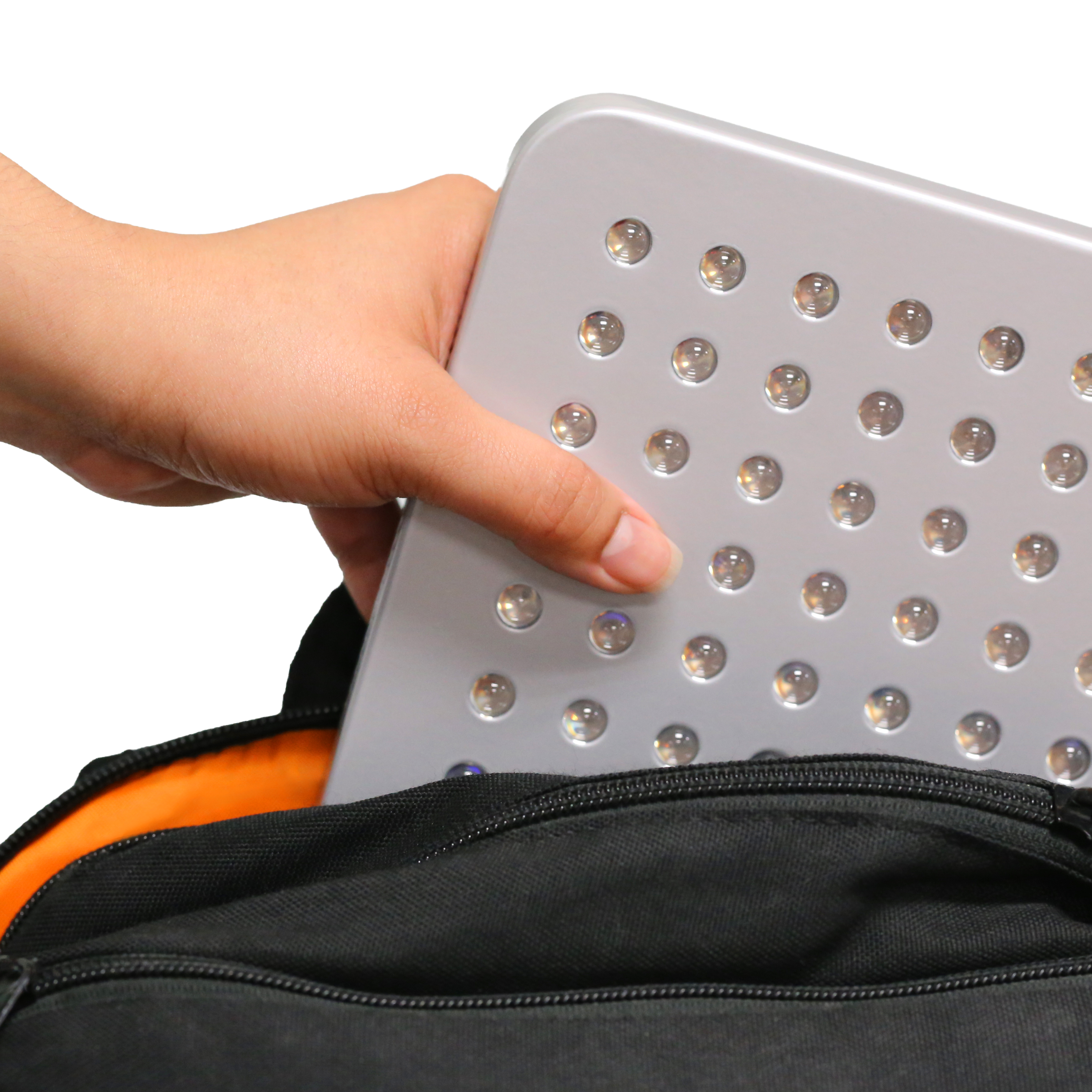 Woman’s hand sliding the UltraThin LED Red Light Therapy Panel into a backpack pocket, demonstrating its lightweight, portable design.