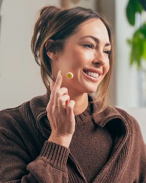 Young woman applying GlowUp LED pimple patch on acne-prone cheek for scar reduction.