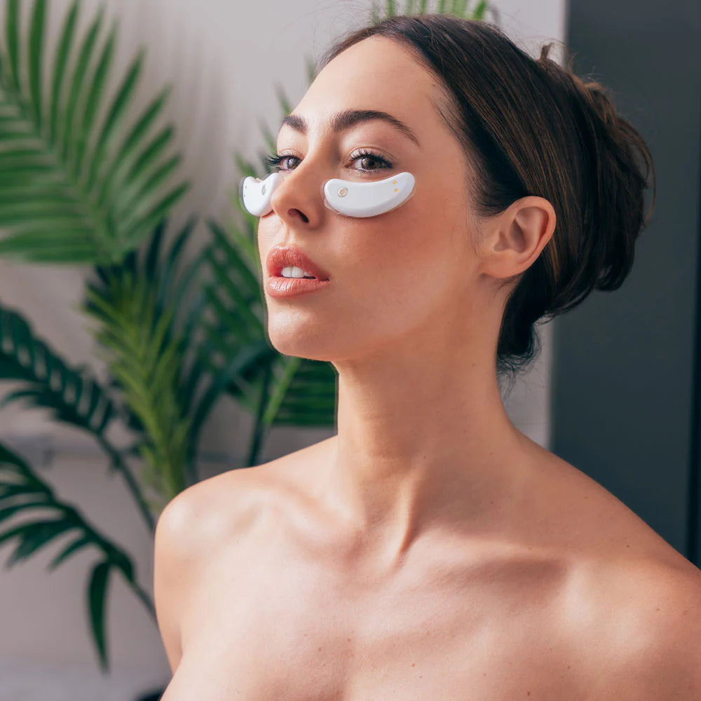 Woman wearing the GlowUp LED/EMS Under Eye Pads beneath her eyes, relaxing while the red light therapy activates for a targeted anti-aging treatment